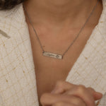 Close-up of a silver bar necklace with a personalized birth flower design and a name engraved as the flower's stem, worn by a woman.