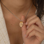 Close-up of a silver pendant necklace featuring a personalized engraving of a plant leaf design worn by a women.