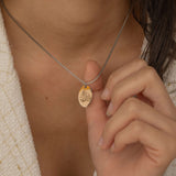 Close-up of a silver pendant necklace featuring a personalized engraving of a plant leaf design worn by a women.