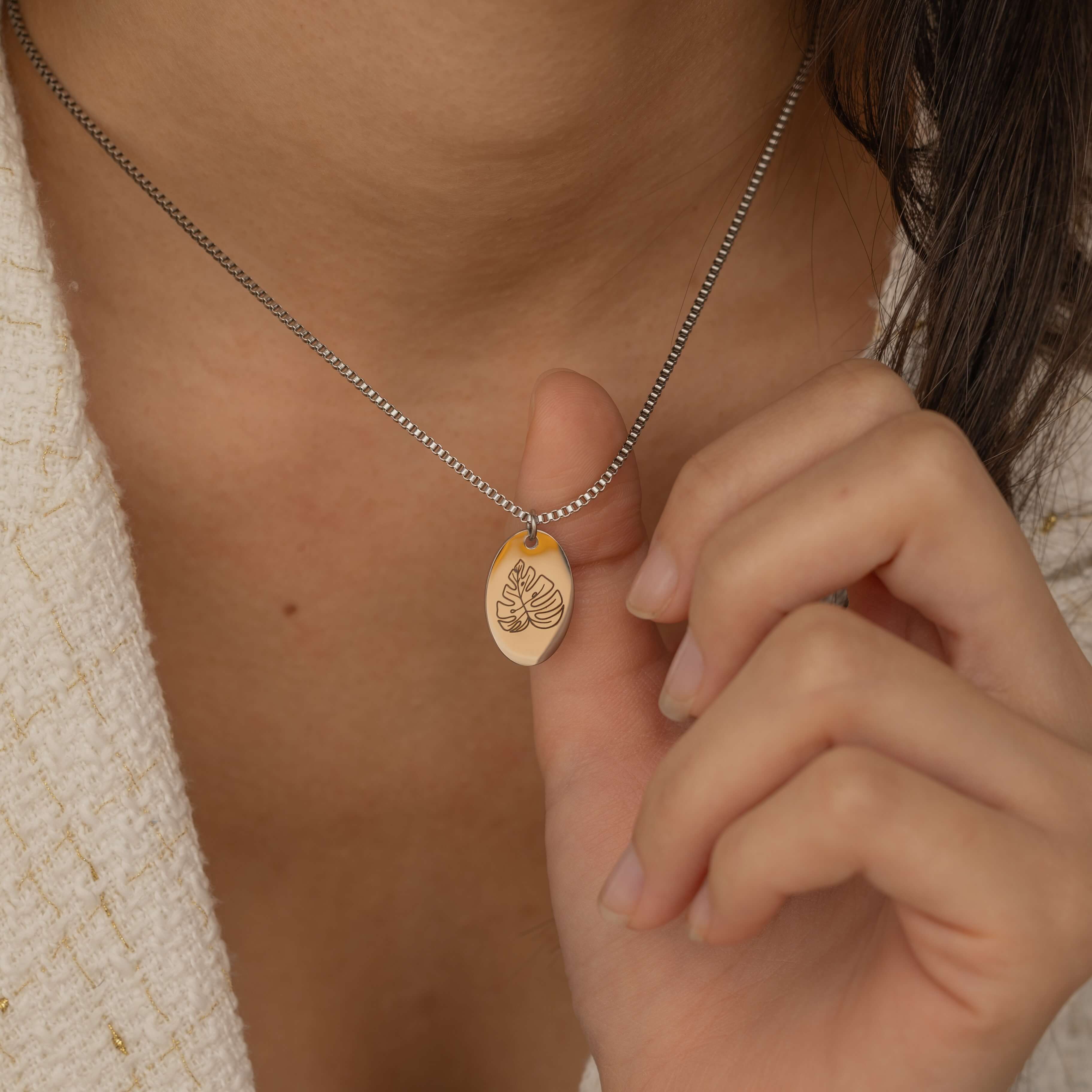 Close-up of a silver pendant necklace featuring a personalized engraving of a plant leaf design worn by a women.