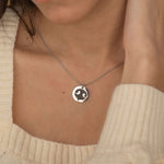 Close-up of a silver pendant necklace featuring an engraved dog nose print design worn by a woman.