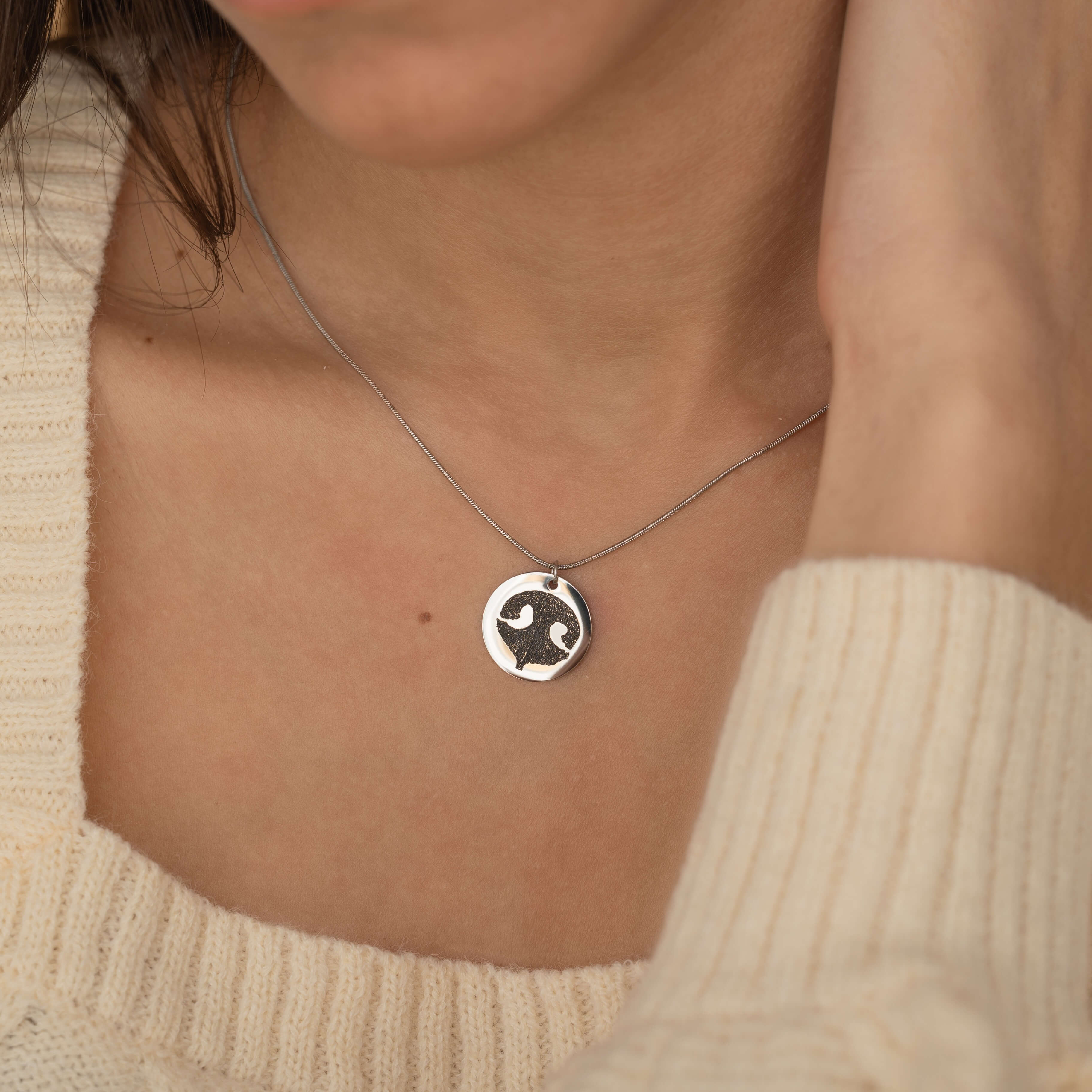 Close-up of a silver pendant necklace featuring an engraved dog nose print design worn by a woman.
