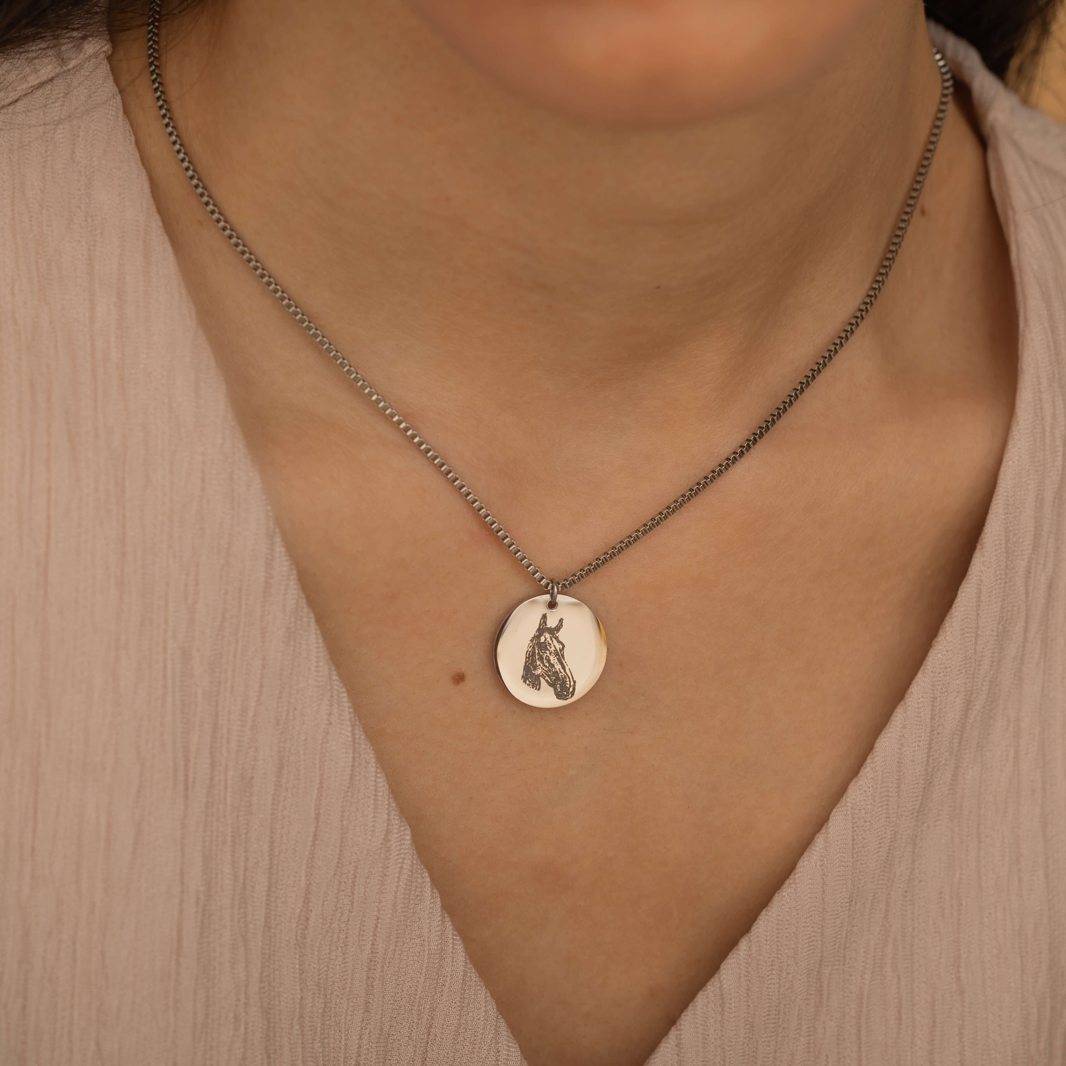 Silver pendant necklace featuring an engraved portrait of a horse worn by a woman