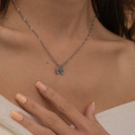 Close-up of a silver necklace with multiple engraved pendants, each featuring different initials, worn by a woman.