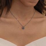 Close-up of a silver necklace with multiple engraved pendants, each featuring different initials, worn by a woman.