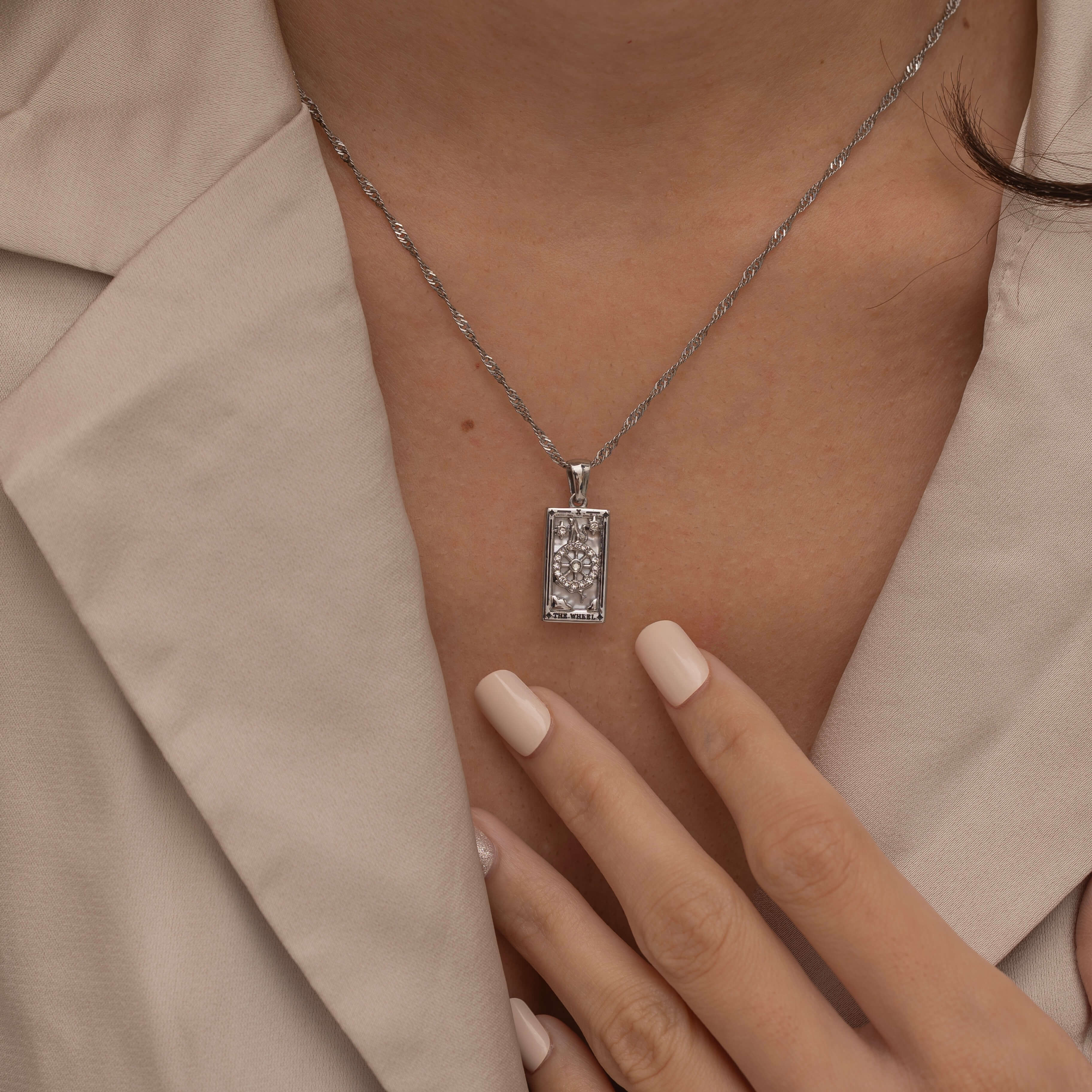 Silver the wheel tarot necklace with cubic zirconia accents and a mother of pearl back stone, symbolizing change, destiny, and the cycles of life. 