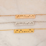 Close-up of three bar necklaces each engraved with a personalized Morse code message, on top of a stone.