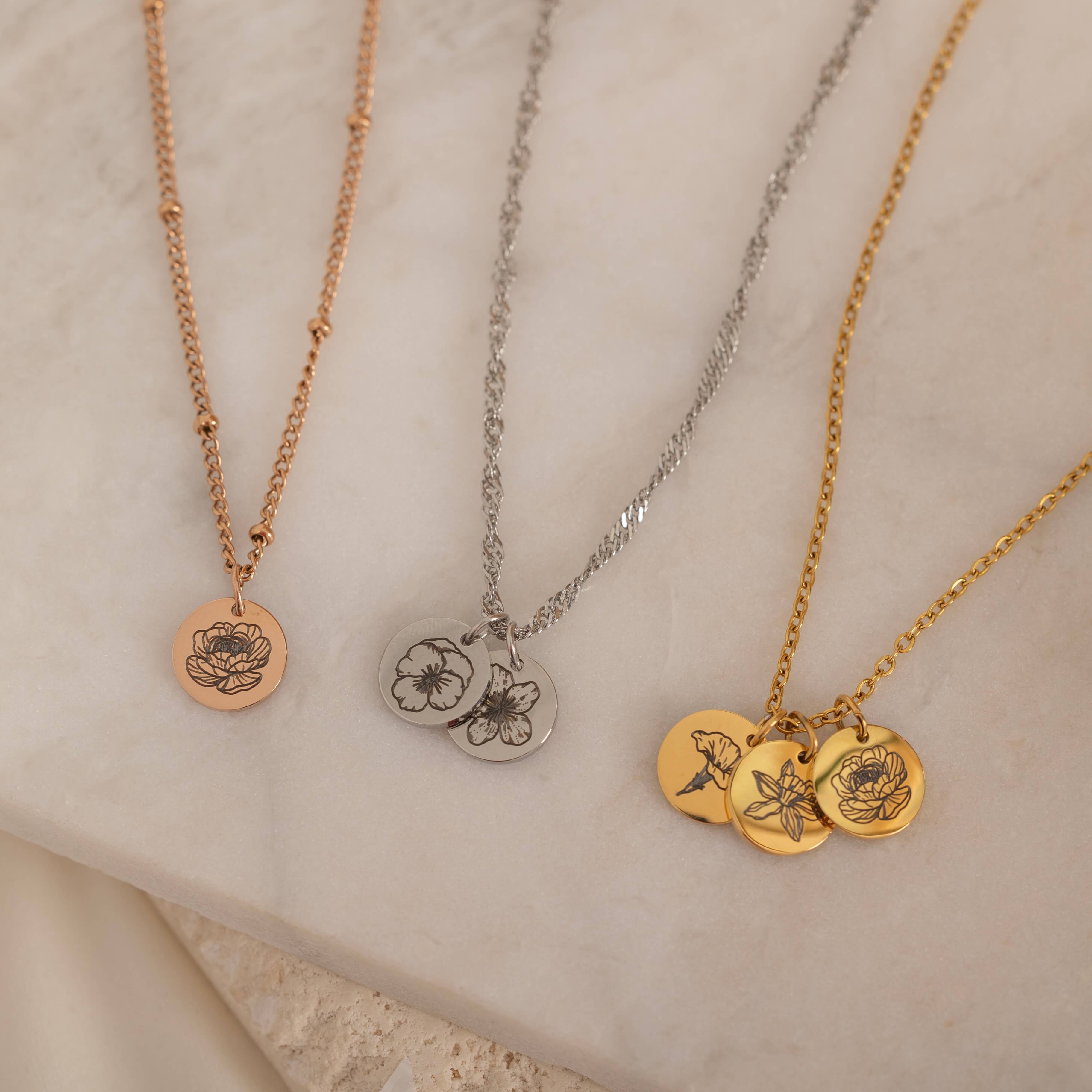 Close-up of three custom birth flower engraved pendant necklace on a decorative stone, showcasing birth flowers