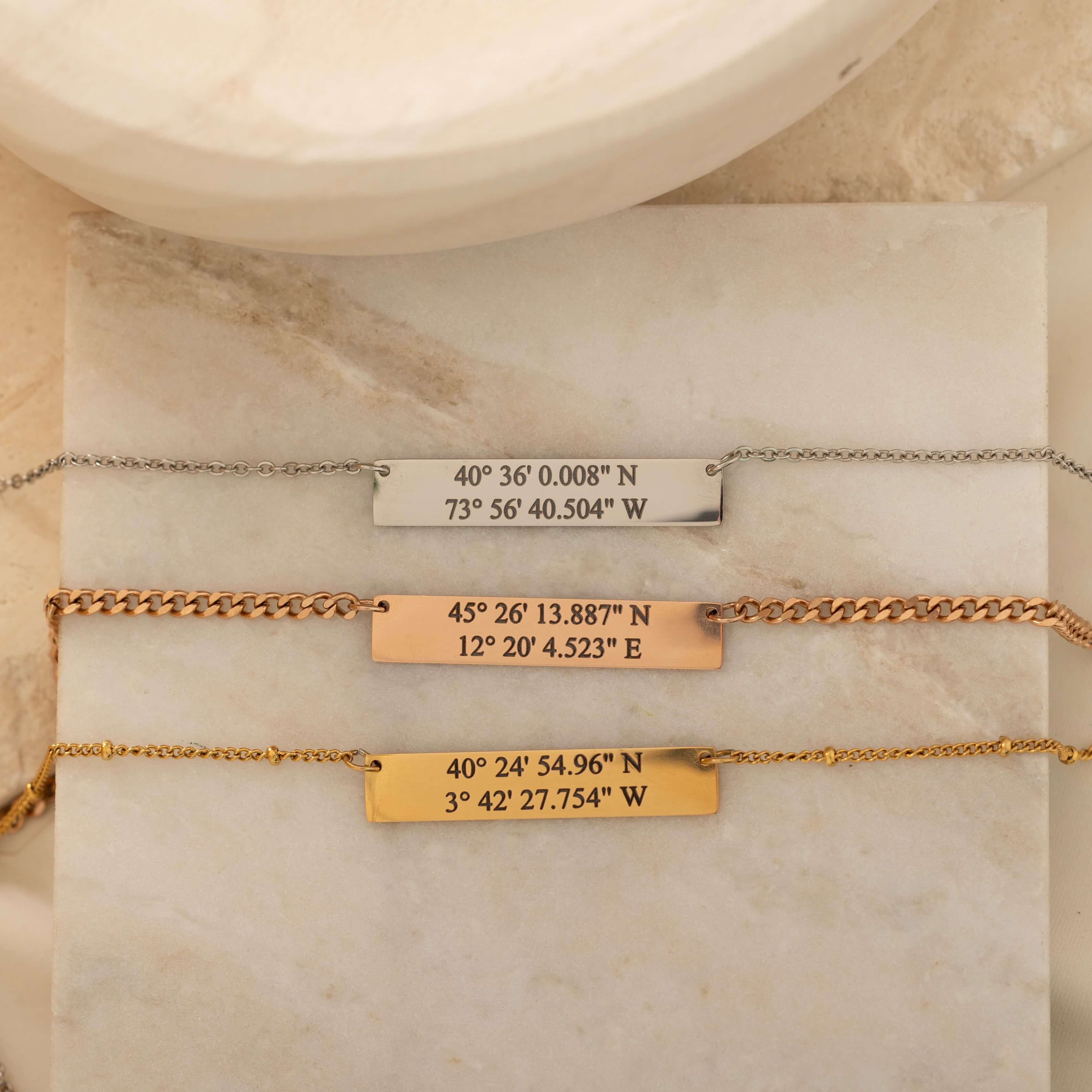 Close-up of three pendant necklace engraved with coordinates on top of a stone.