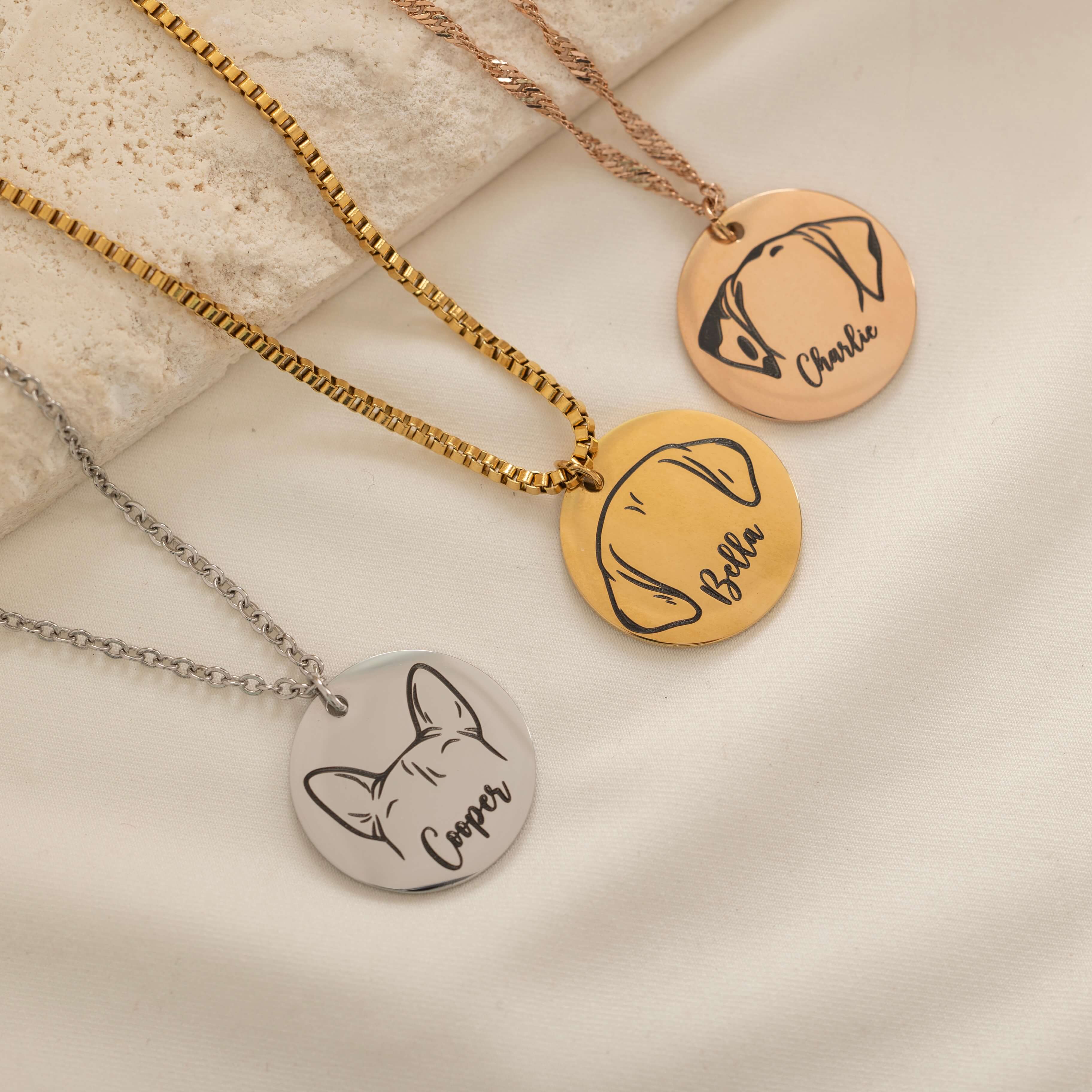 Three pendant necklace featuring an engraved outline of dog ears with a pet's name underneath, on top of a stone.