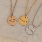 Close-up of a three round pendant necklace engraved with the handwritten messages on top of a stone