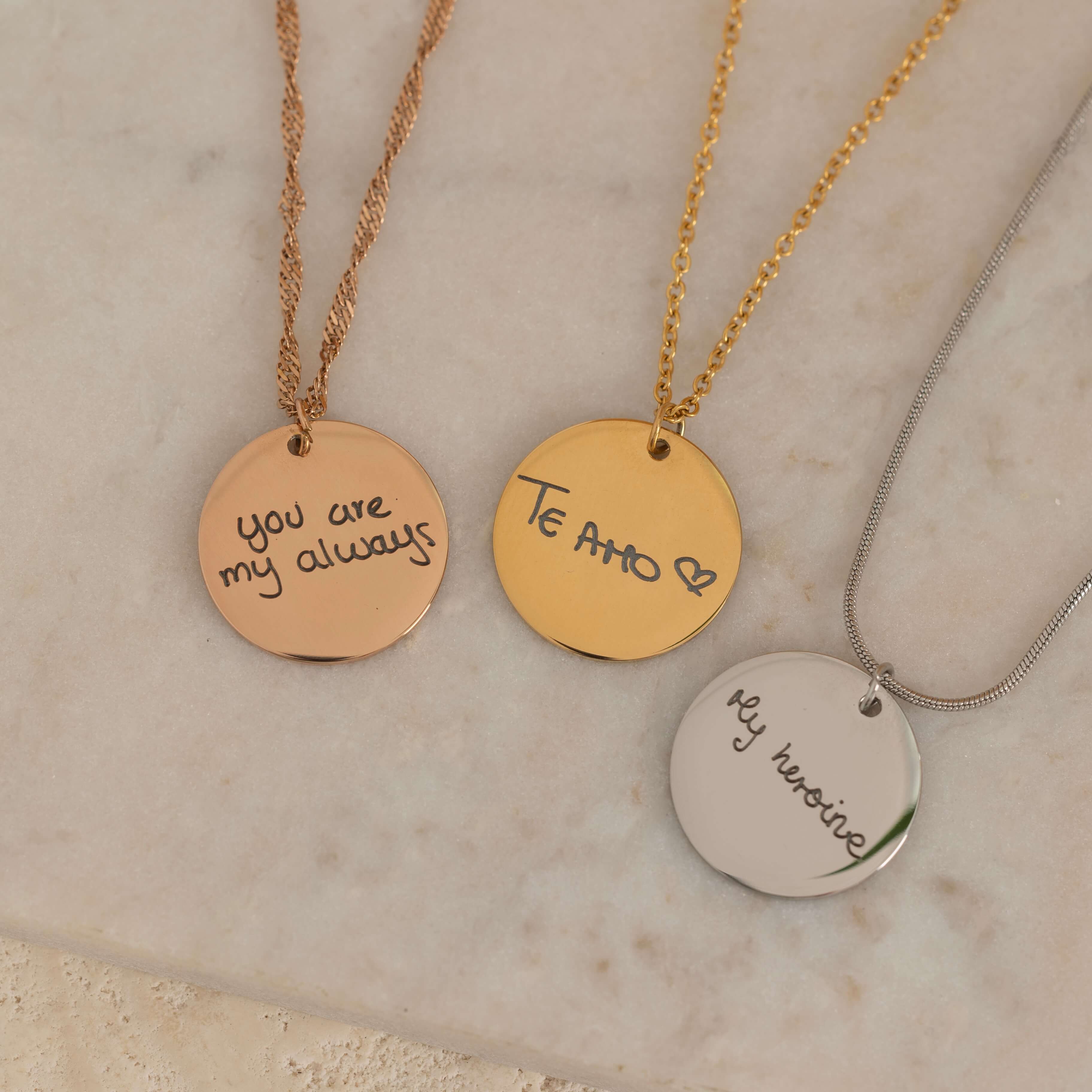Close-up of a three round pendant necklace engraved with the handwritten messages on top of a stone
