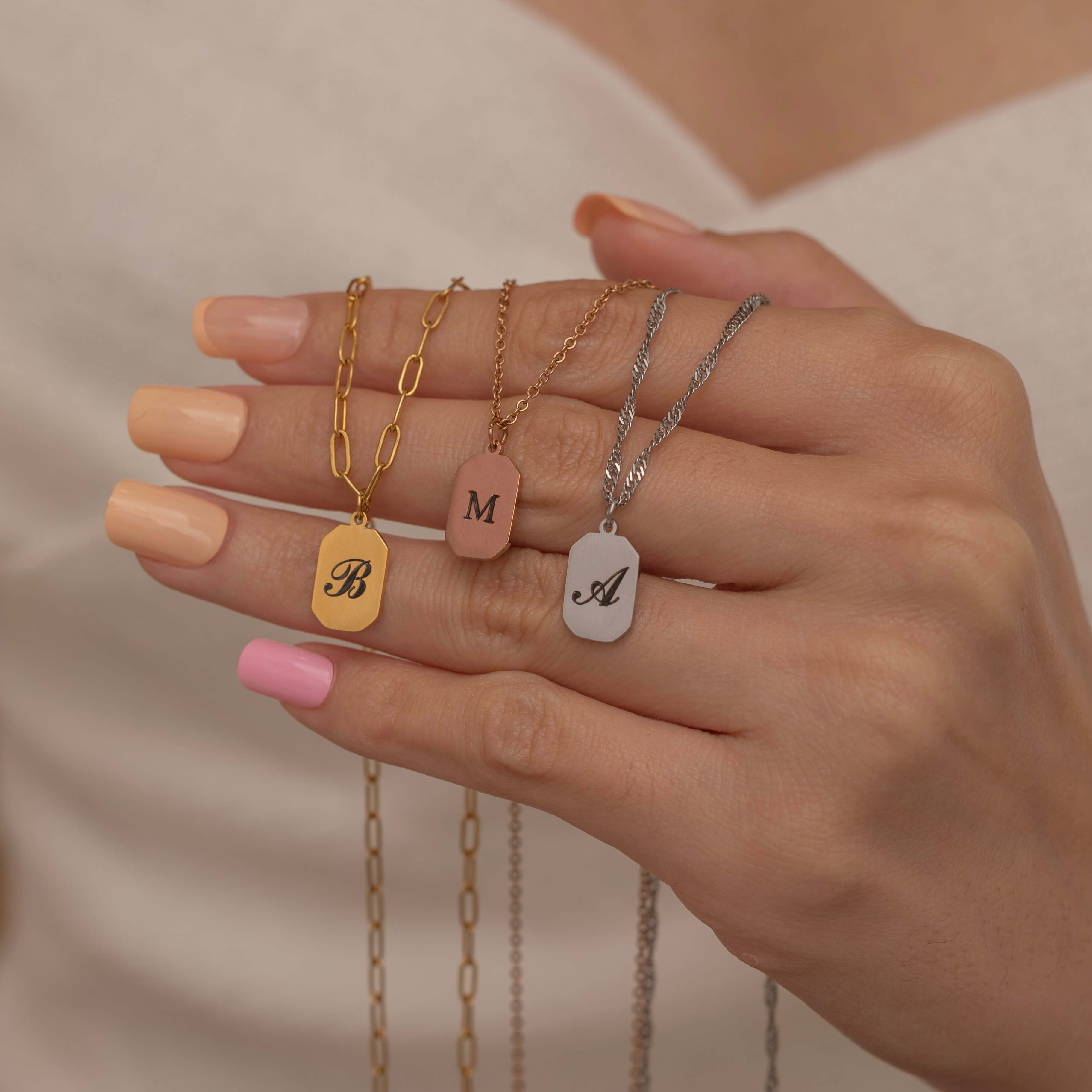 Women hand holding three letter initial necklaces in gold, rose gold, and silver 