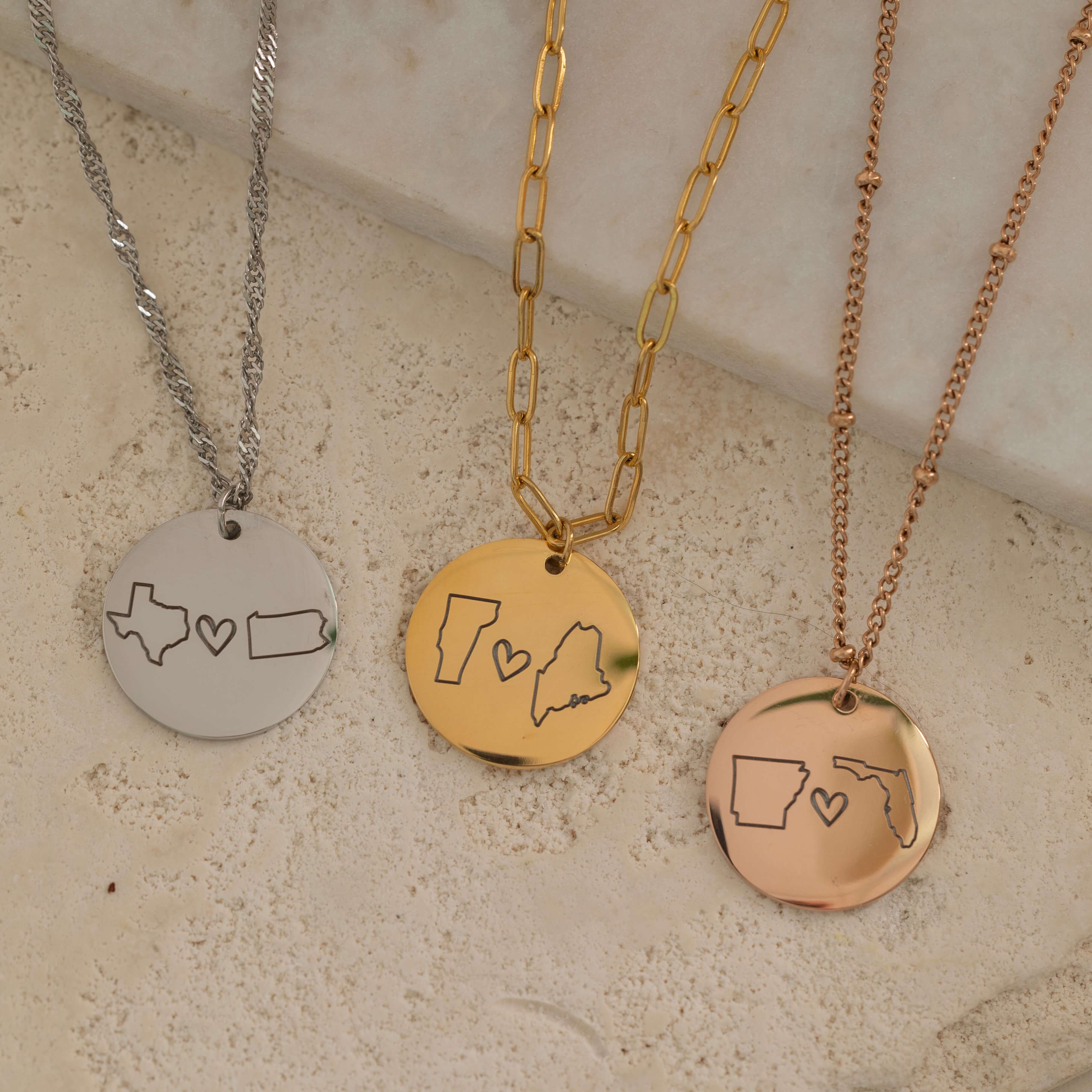 Close-up of three pendant necklace engraved with two state outlines and a heart in the center each, on top of a stone