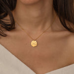 Close-up of a gold pendant necklace engraved with two state outlines and a heart in the center, worn by a woman.