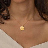 Close-up of a gold pendant necklace engraved with two state outlines and a heart in the center, worn by a woman.