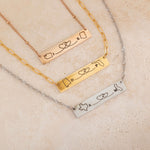 Close-up of three bar necklace each engraved with two state outlines at each corner and a heart in the middle connecting them, on top of a stone.