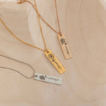 Close-up of a pendant necklaces featuring an engraved birth flower with a personalized name as the stem.