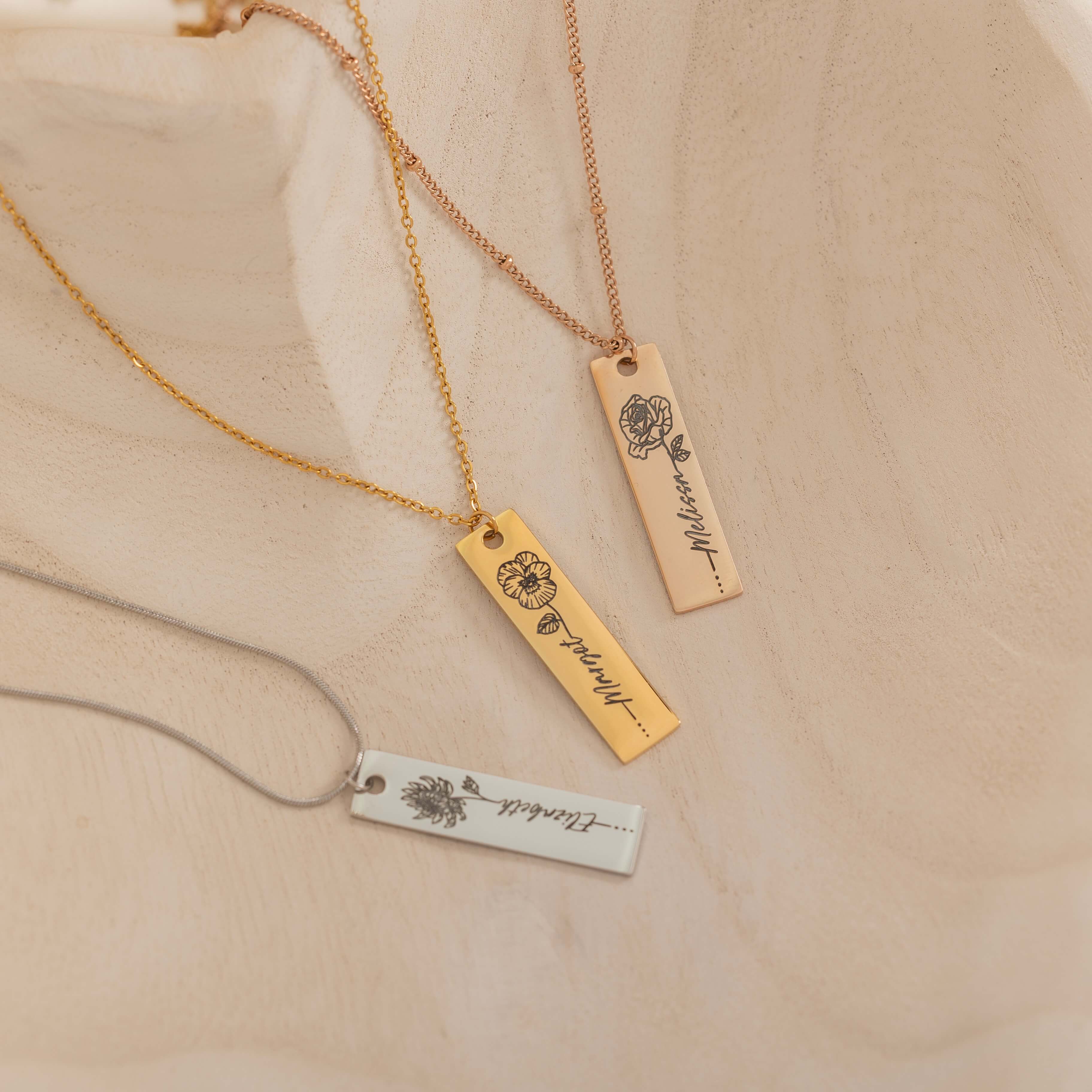 Close-up of a pendant necklaces featuring an engraved birth flower with a personalized name as the stem.