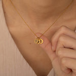 Close-up of a gold custom birth flower engraved pendant necklace worn by a woman, showcasing three round charms with floral engravings being held between fingers.