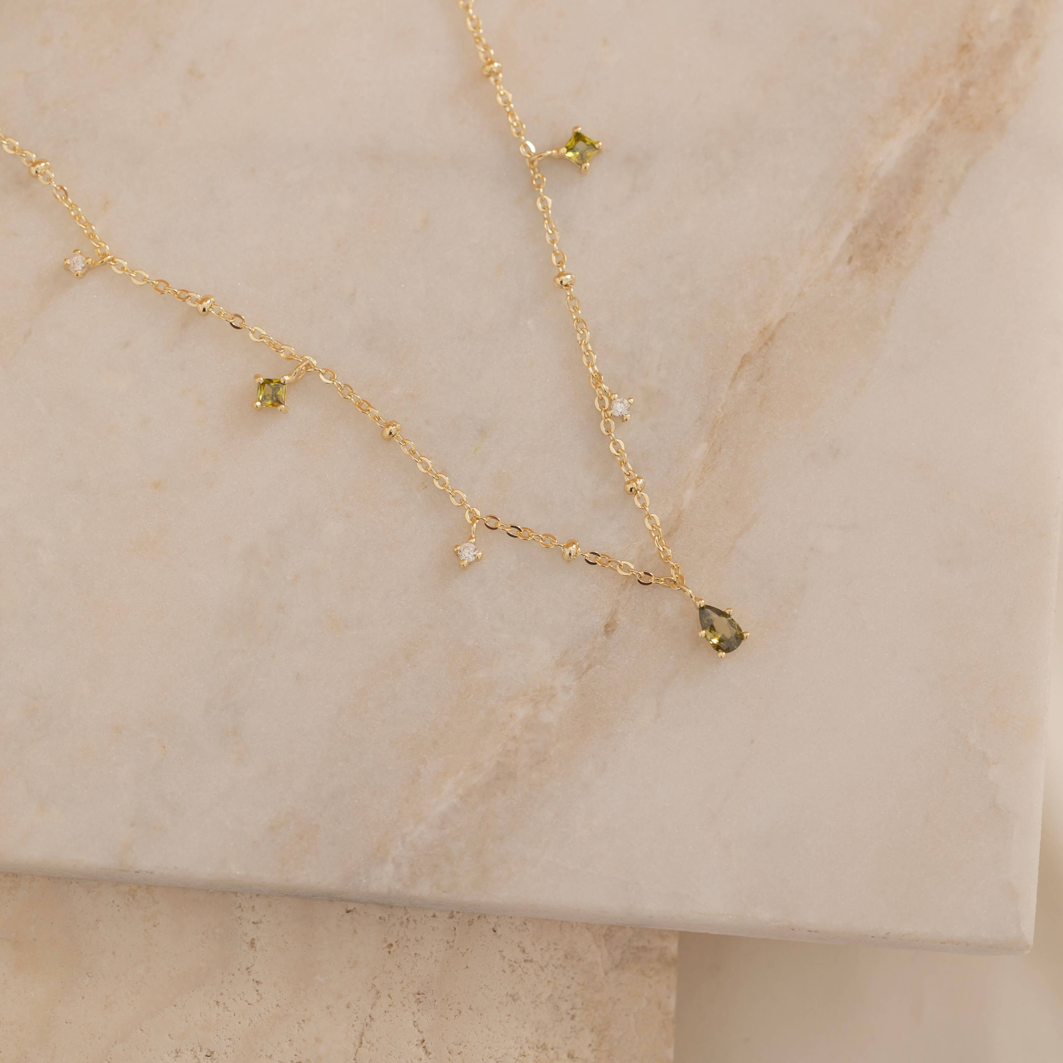 Dainty sterling silver and 14k gold plated necklace featuring four square peridot-colored cubic zirconia stones, one centered teardrop-shaped peridot stone, and four white cubic zirconia accents between the peridot.