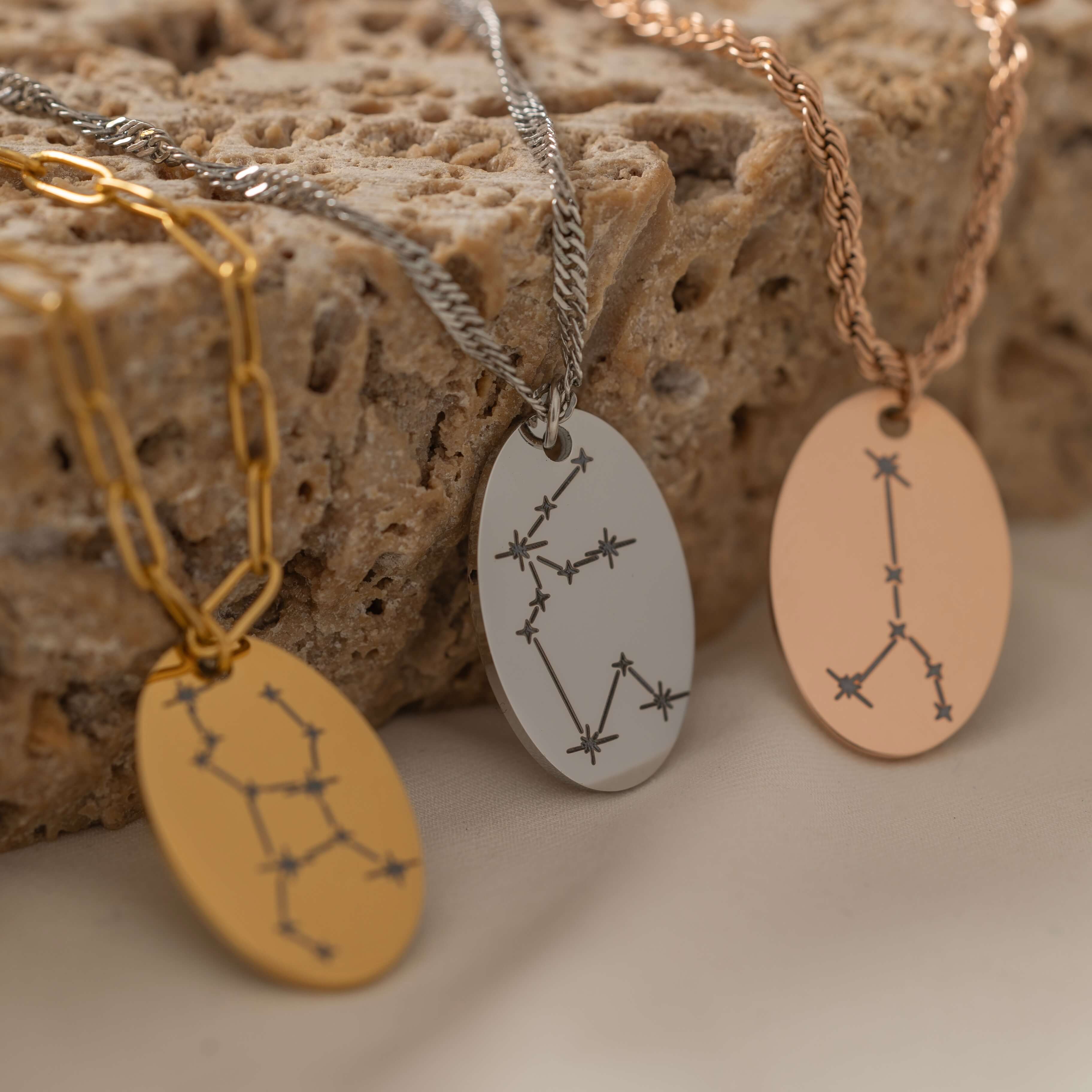 Close-up of pendant necklaces featuring engraved zodiac constellations designs.