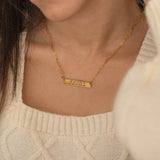 Close-up of a gold pendant necklace engraved with coordinates worn by a woman.