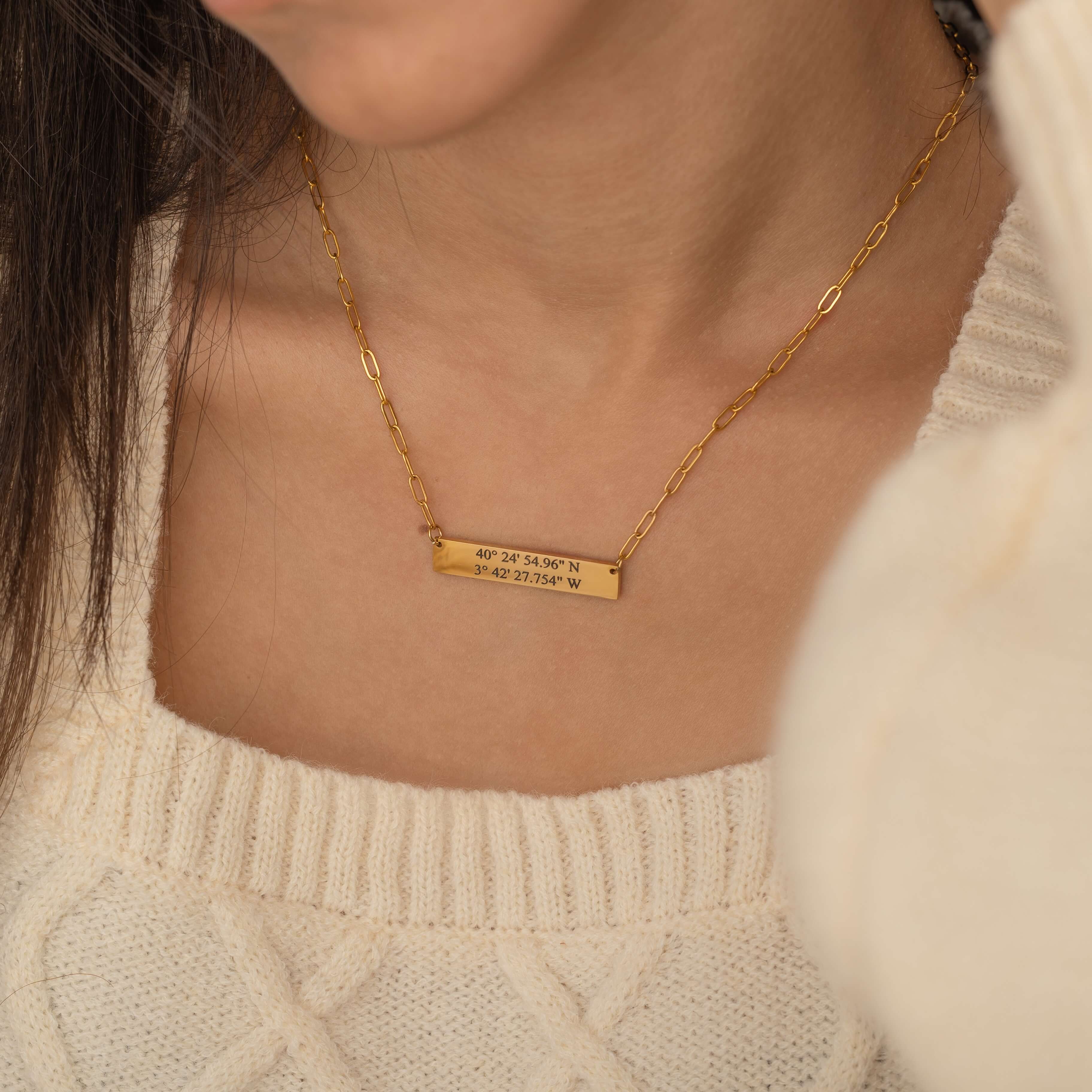 Close-up of a gold pendant necklace engraved with coordinates worn by a woman.