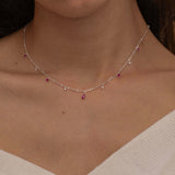 Dainty sterling silver necklace featuring four square pink ruby-colored cubic zirconia stones, one centered teardrop-shaped pink ruby stone, and four white cubic zirconia accents between the pink ruby. 