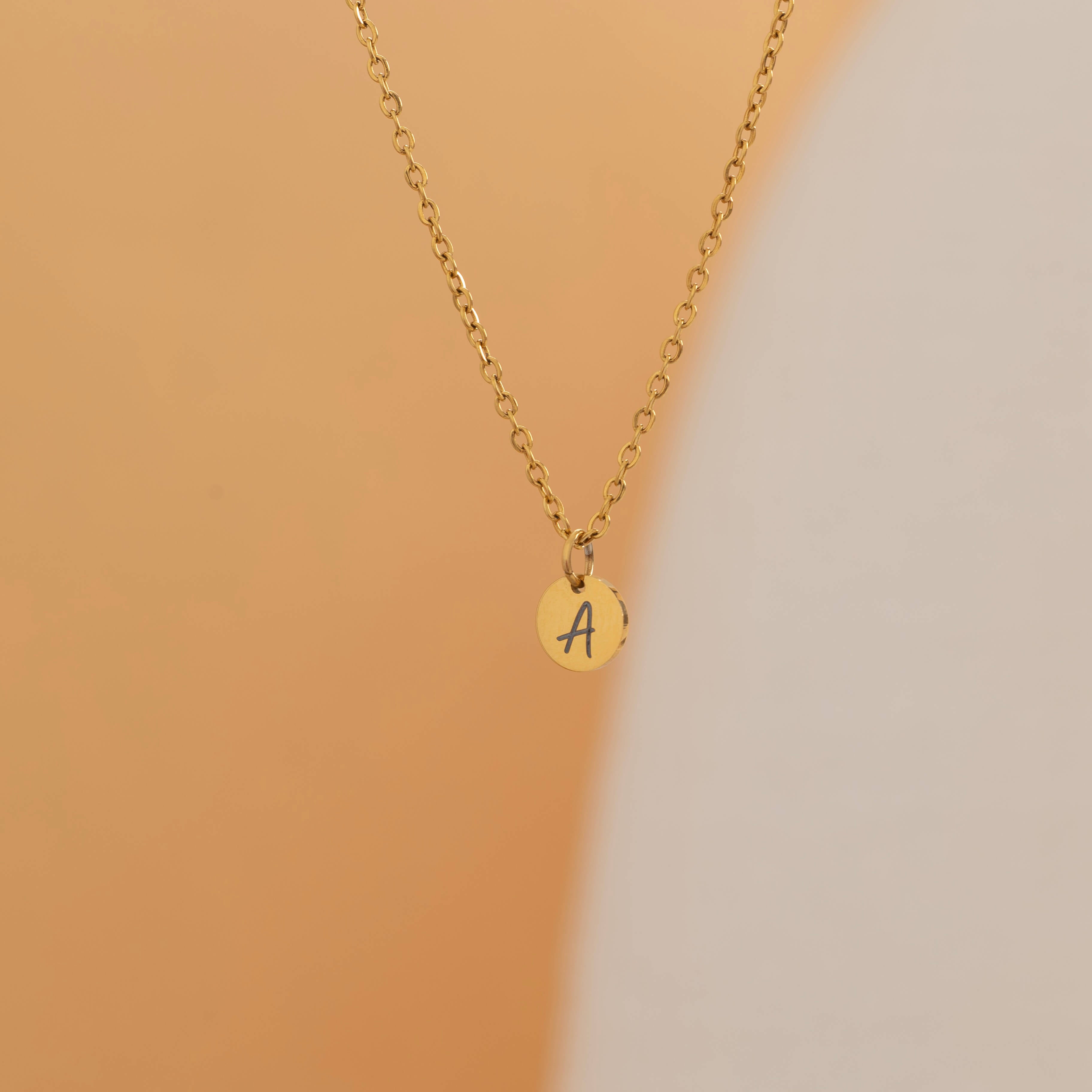 custom initial charm necklaces in gold, silver, and rose gold finishes, each with distinct chain styles and personalized round charms on a marble surface.