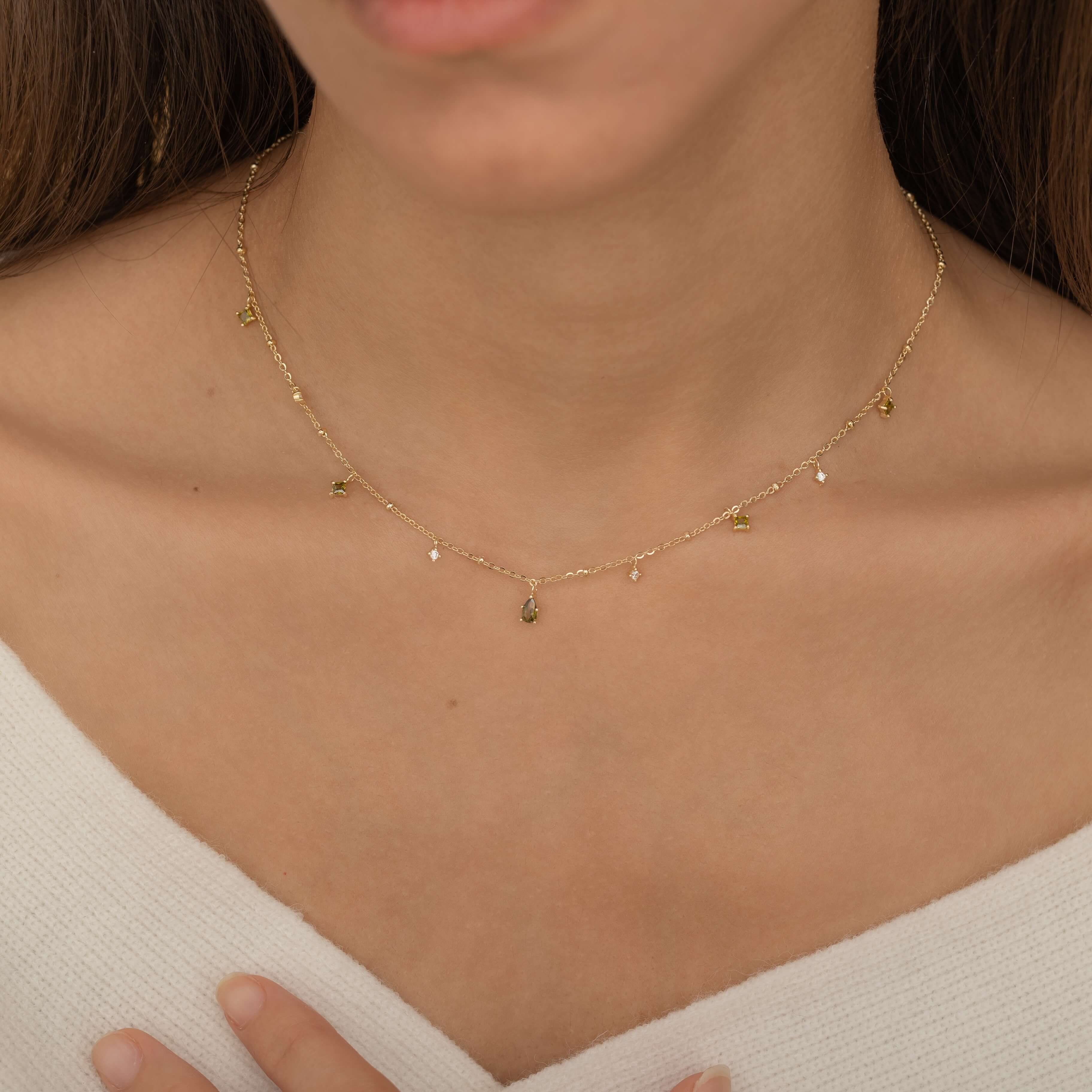 Dainty sterling silver and 14k gold plated necklace featuring four square peridot-colored cubic zirconia stones, one centered teardrop-shaped peridot stone, and four white cubic zirconia accents between the peridot.