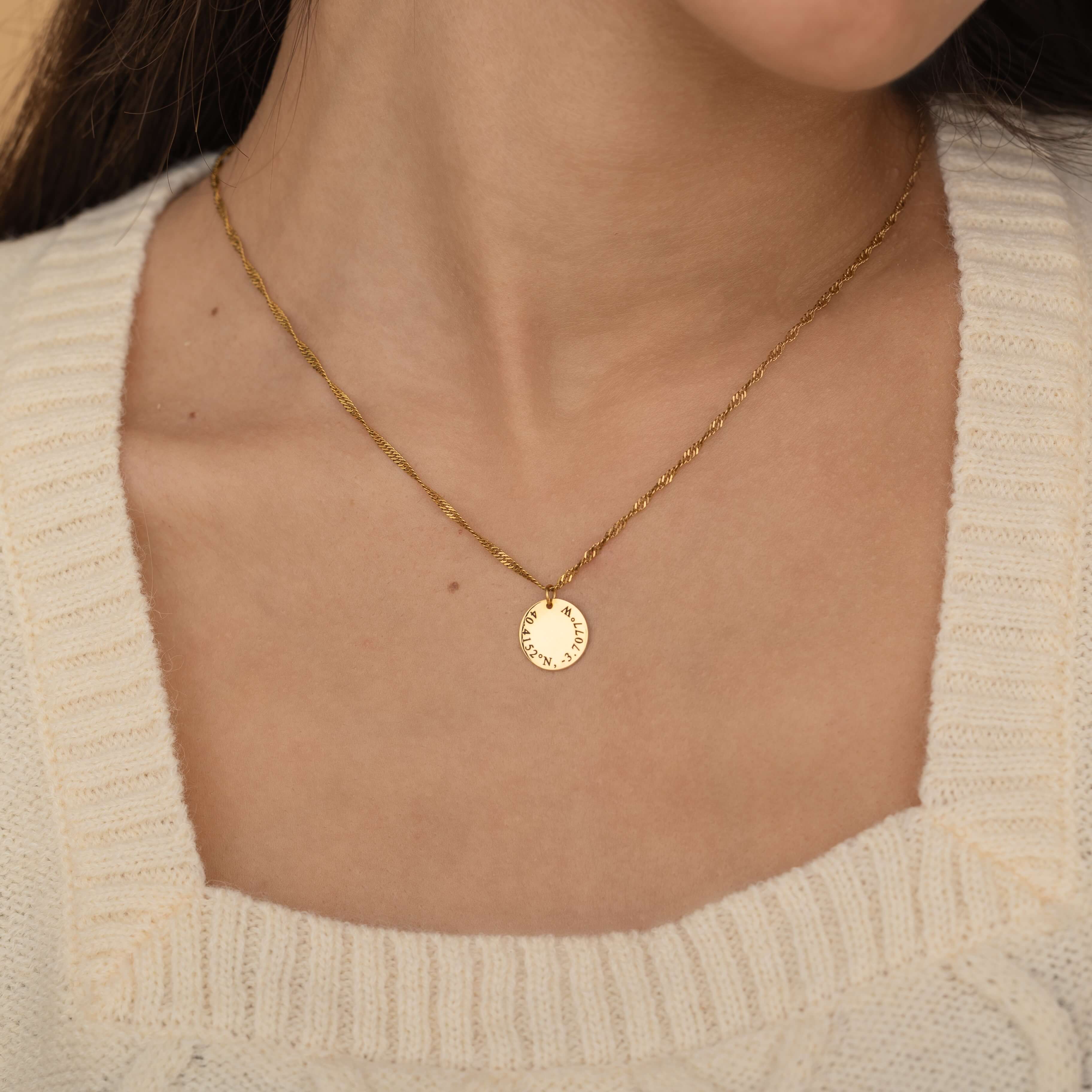 Close-up of a silver custom coordinate necklace worn on a woman's neck, featuring engraved latitude and longitude details on a round pendant.