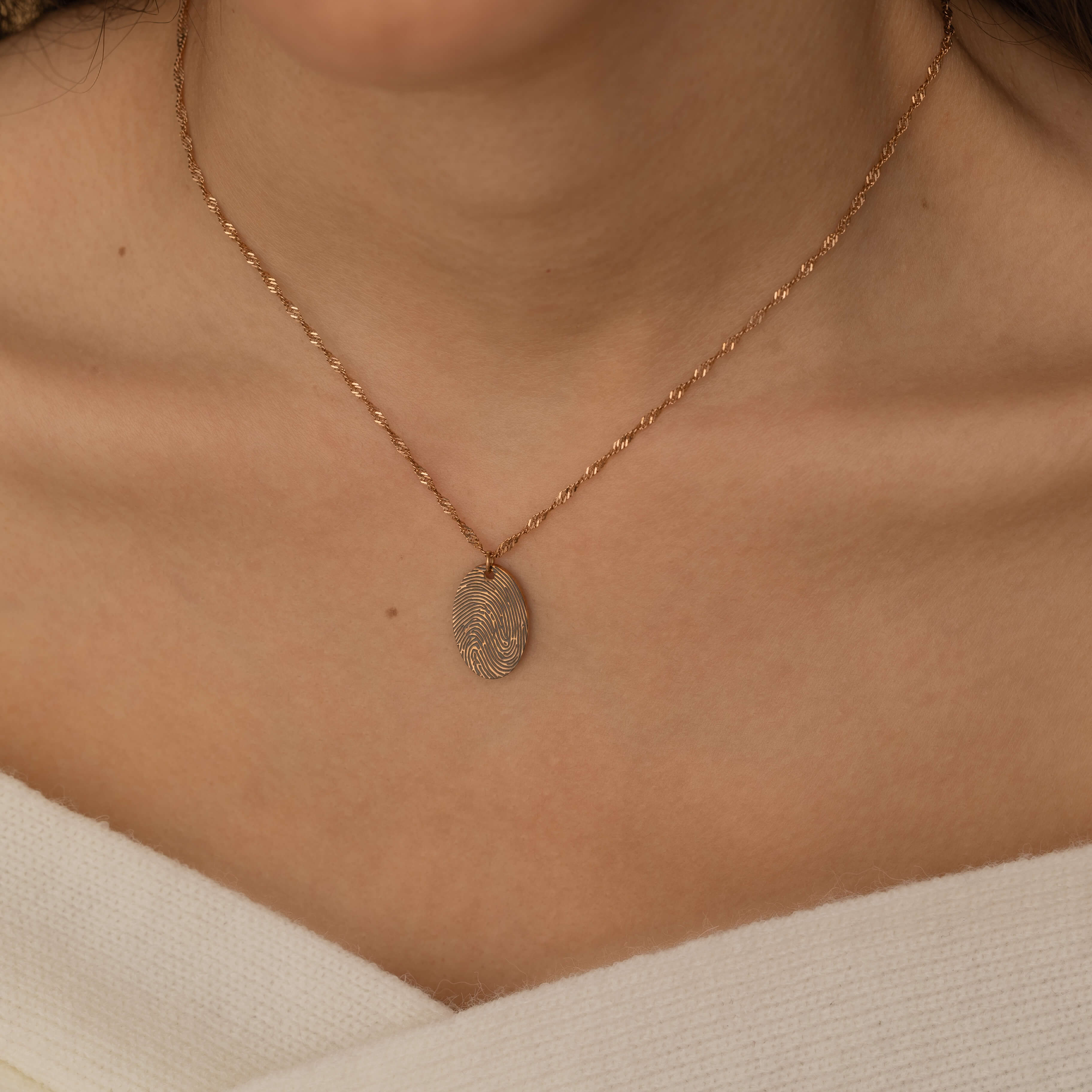 Close-up of a rose gold pendant necklace engraved with a personalized fingerprint, worn by a woman.
