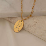 Close-up of a gold pendant necklace featuring an engraved zodiac constellation design.