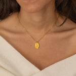 Close-up of a gold pendant necklace featuring an engraved zodiac constellation design worn by a women.