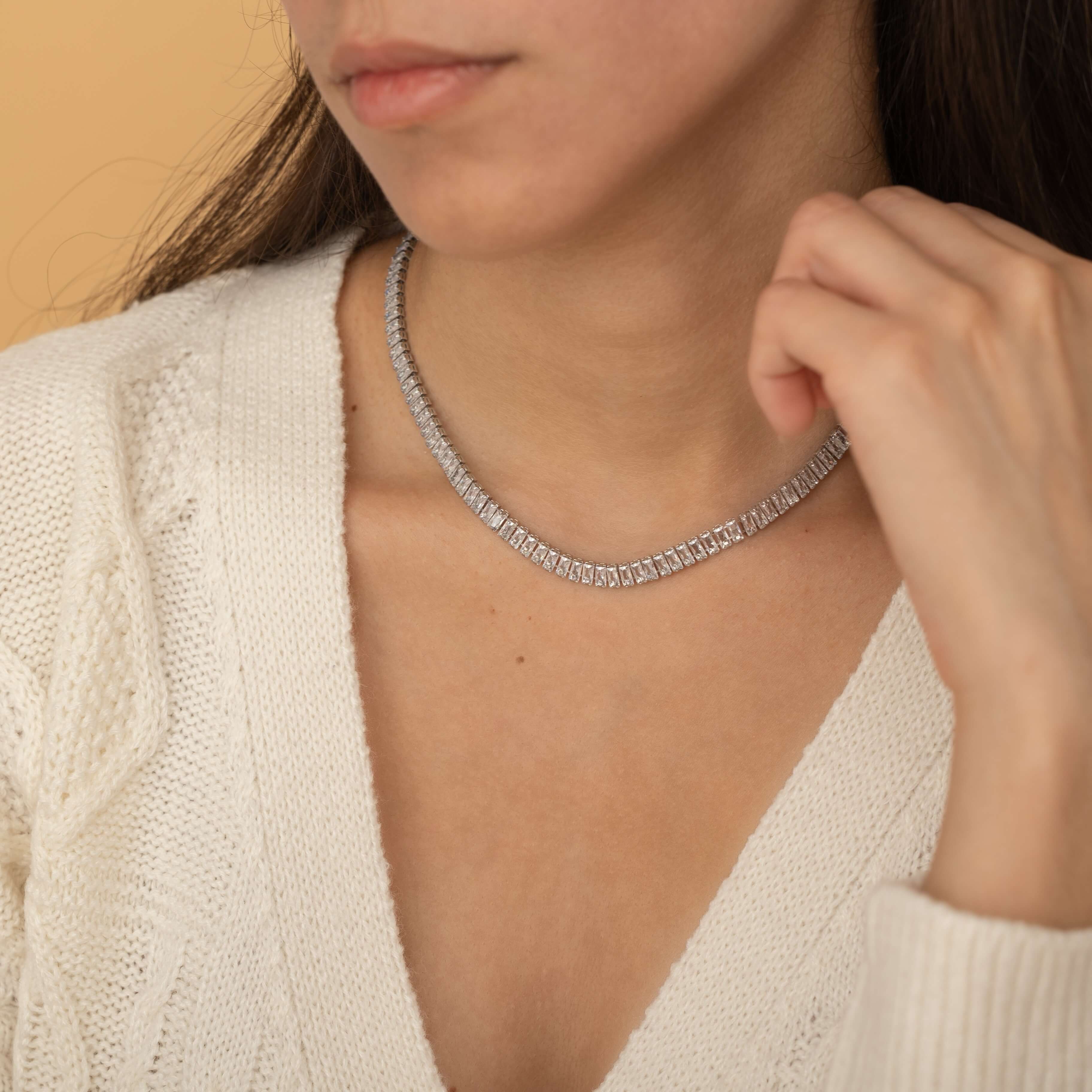 Elegant gold tennis necklace with a continuous row of sparkling, rectangular-cut stones. Perfectly aligned gemstones create a seamless shimmer, adding timeless sophistication to any look. Classic luxury jewelry piece ideal for formal occasions or adding everyday elegance.