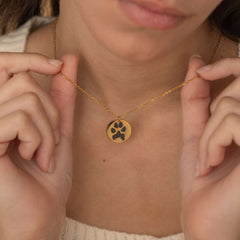 Close-up of a gold pendant necklace featuring an engraved dog paw design being held by a women.