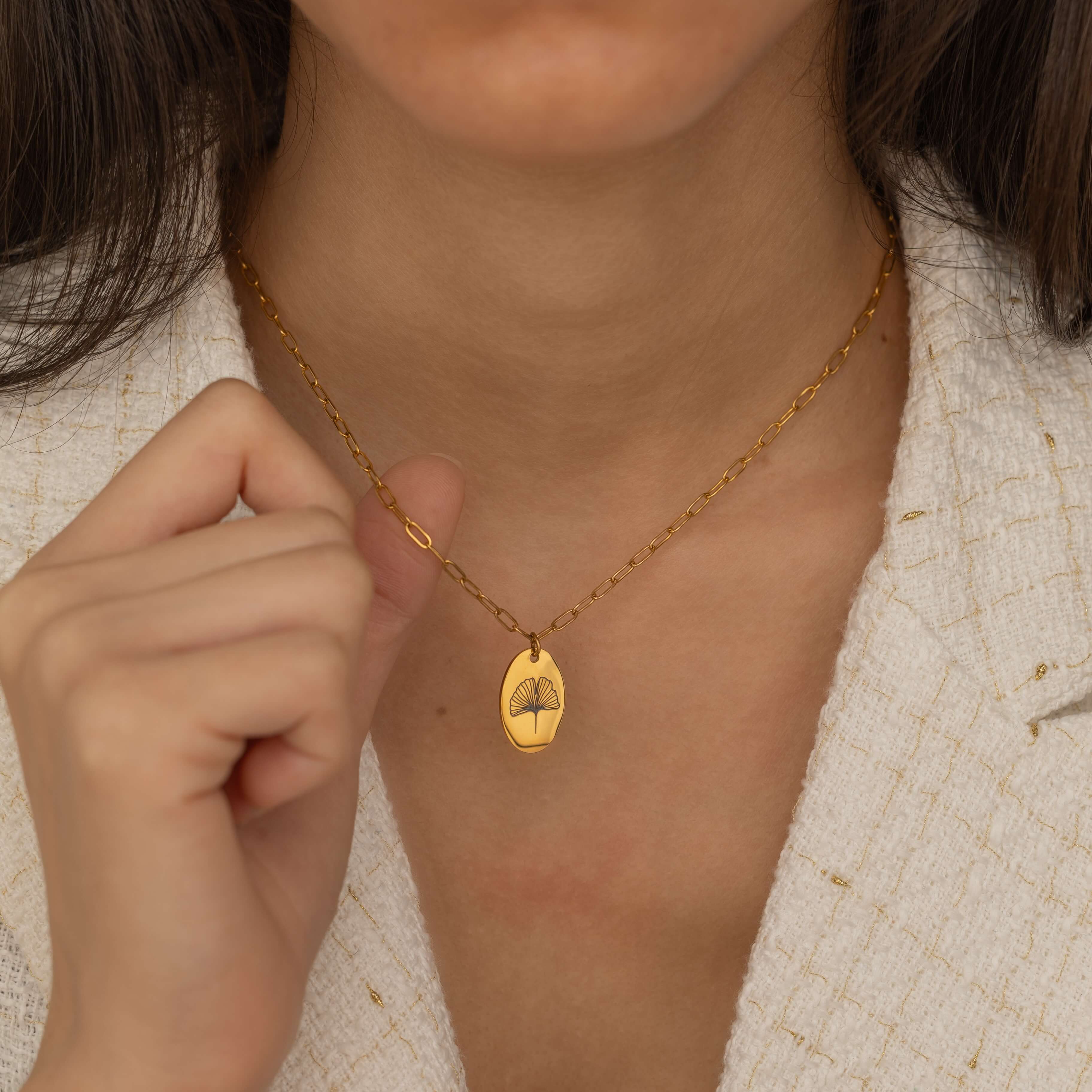 Close-up of a gold pendant necklace featuring a personalized engraving of a plant leaf design.