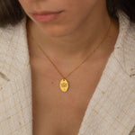 Close-up of a gold pendant necklace featuring a personalized engraving of a plant leaf design worn by a women.