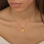 Close-up of a gold necklace engraved with a birth flower representing family member, worn by a woman.