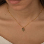 Close-up of a gold pendant engraved with a fingerprint on the front, customizable with a birth flower or text on the back, worn by a woman.