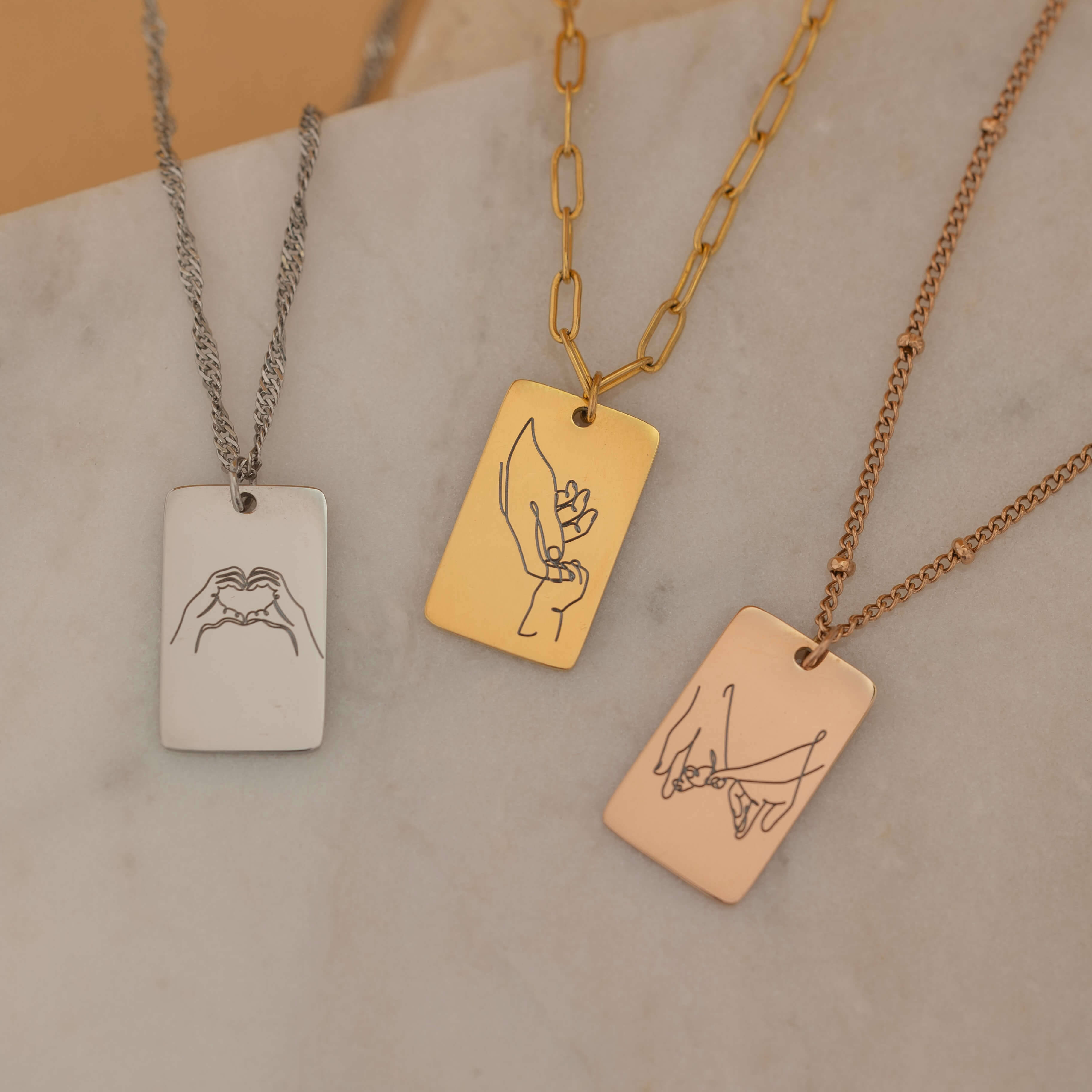 custom hand sign symbol necklaces in gold, silver, and rose gold with engraved rectangular pendants featuring various hand sign designs.