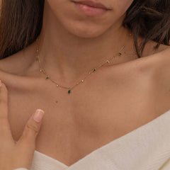 Dainty sterling silver and 14k gold plated necklace featuring four square emerald-colored cubic zirconia stones, one centered teardrop-shaped emerald stone, and four white cubic zirconia accents between the emeralds.