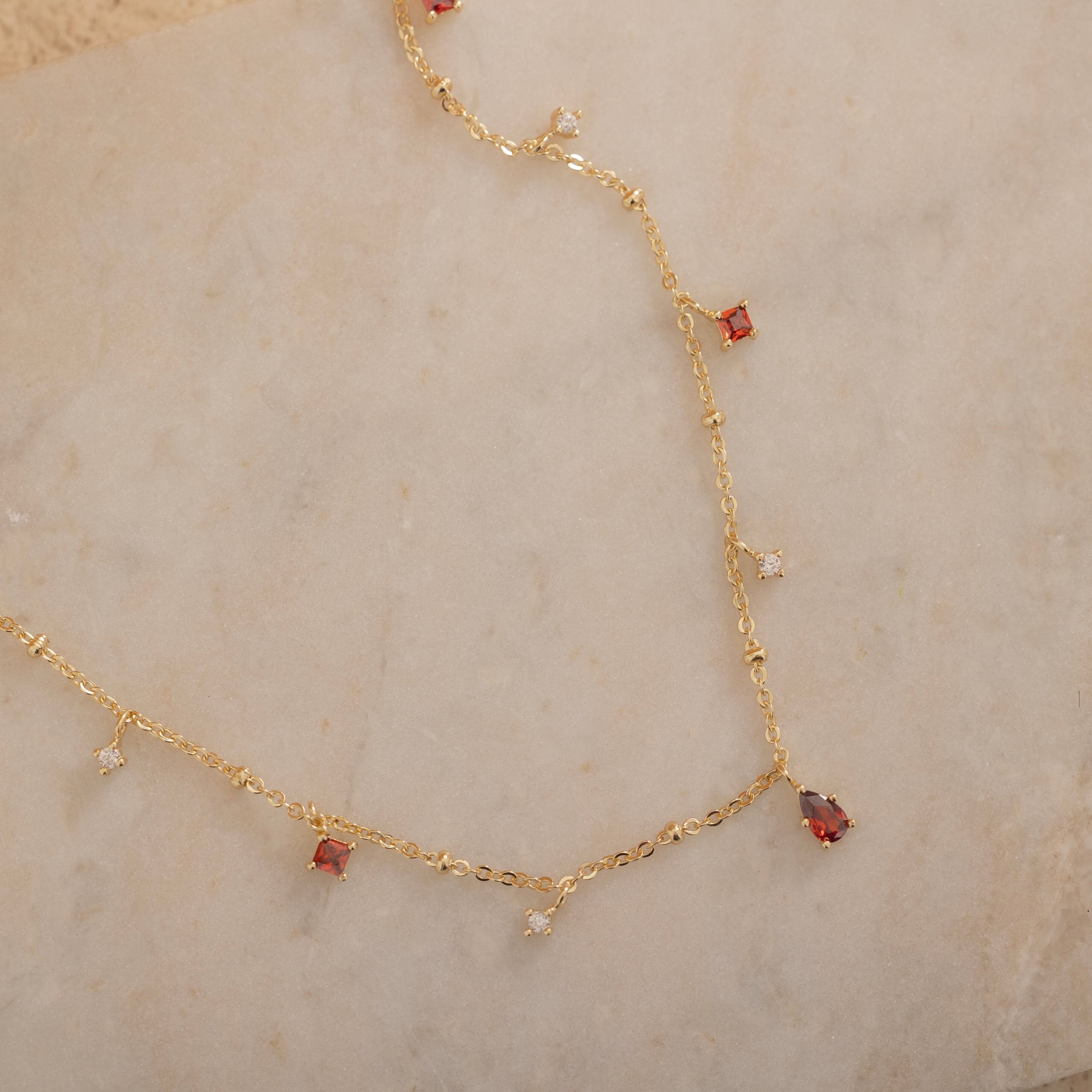 Dainty sterling silver necklace and 14k gold plated featuring four square garnet-colored cubic zirconia stones, one centered teardrop-shaped garnet stone, and four white cubic zirconia accents between the garnet.