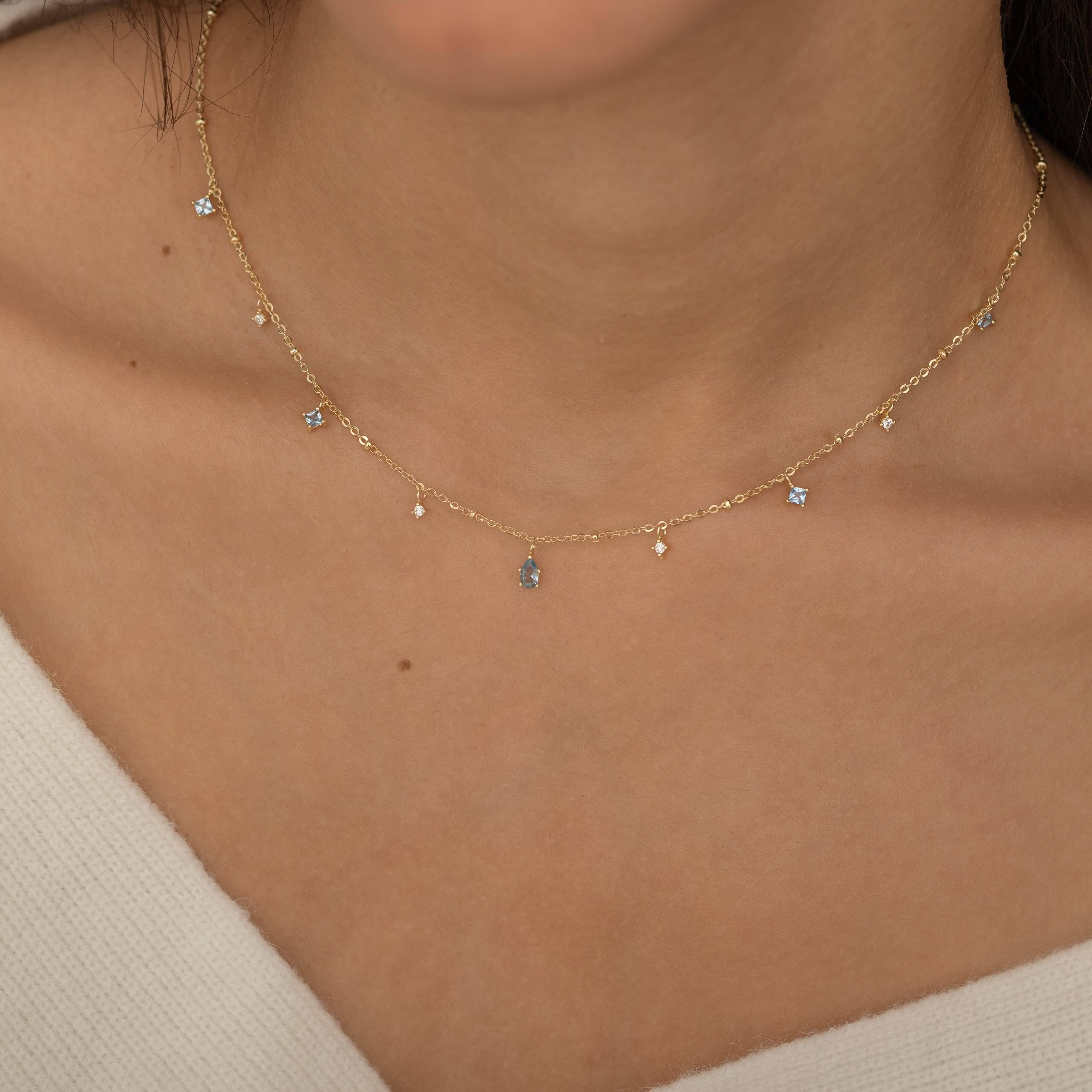 Dainty sterling silver and 14k gold plated necklace featuring four square aquamarine-colored cubic zirconia stones, one centered teardrop-shaped aquamarine stone, and four white cubic zirconia accents between the aquamarine.