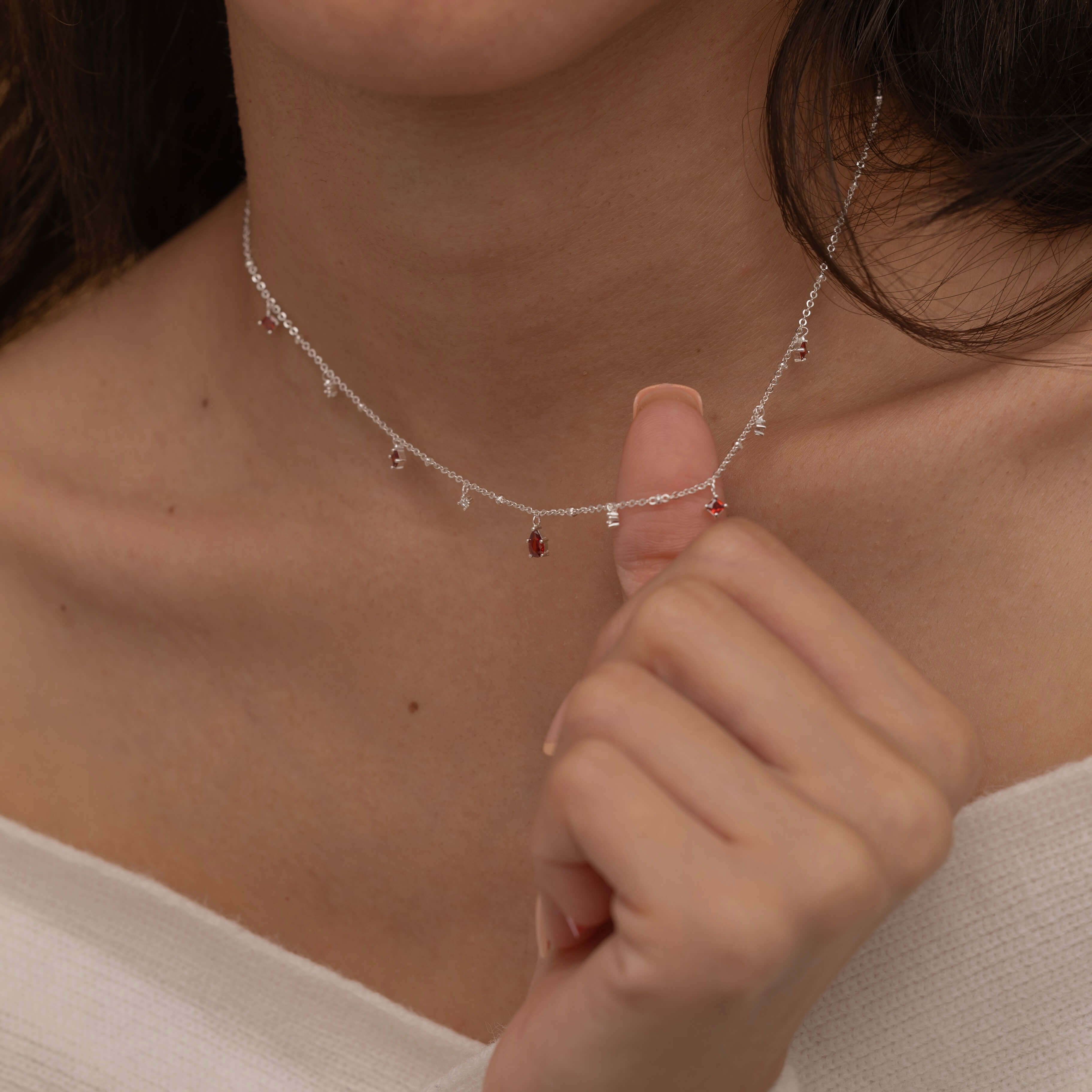 Dainty sterling silver necklace featuring four square garnet-colored cubic zirconia stones, one centered teardrop-shaped garnet stone, and four white cubic zirconia accents between the garnet.