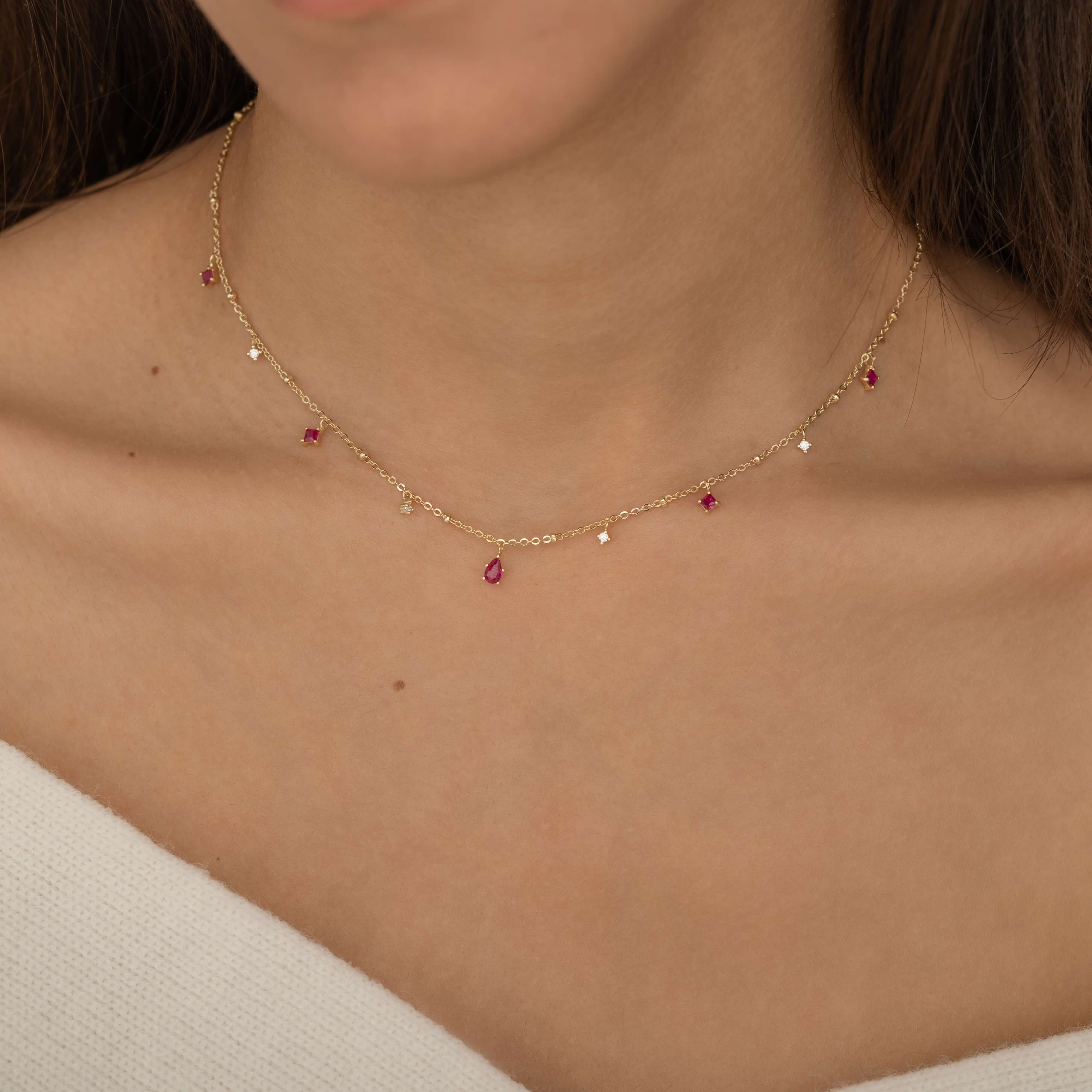 Dainty sterling silver and 14k gold plated necklace featuring four square pink ruby-colored cubic zirconia stones, one centered teardrop-shaped pink ruby stone, and four white cubic zirconia accents between the pink ruby. 