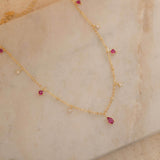 Dainty sterling silver and 14k gold plated necklace featuring four square pink ruby-colored cubic zirconia stones, one centered teardrop-shaped pink ruby stone, and four white cubic zirconia accents between the pink ruby. 