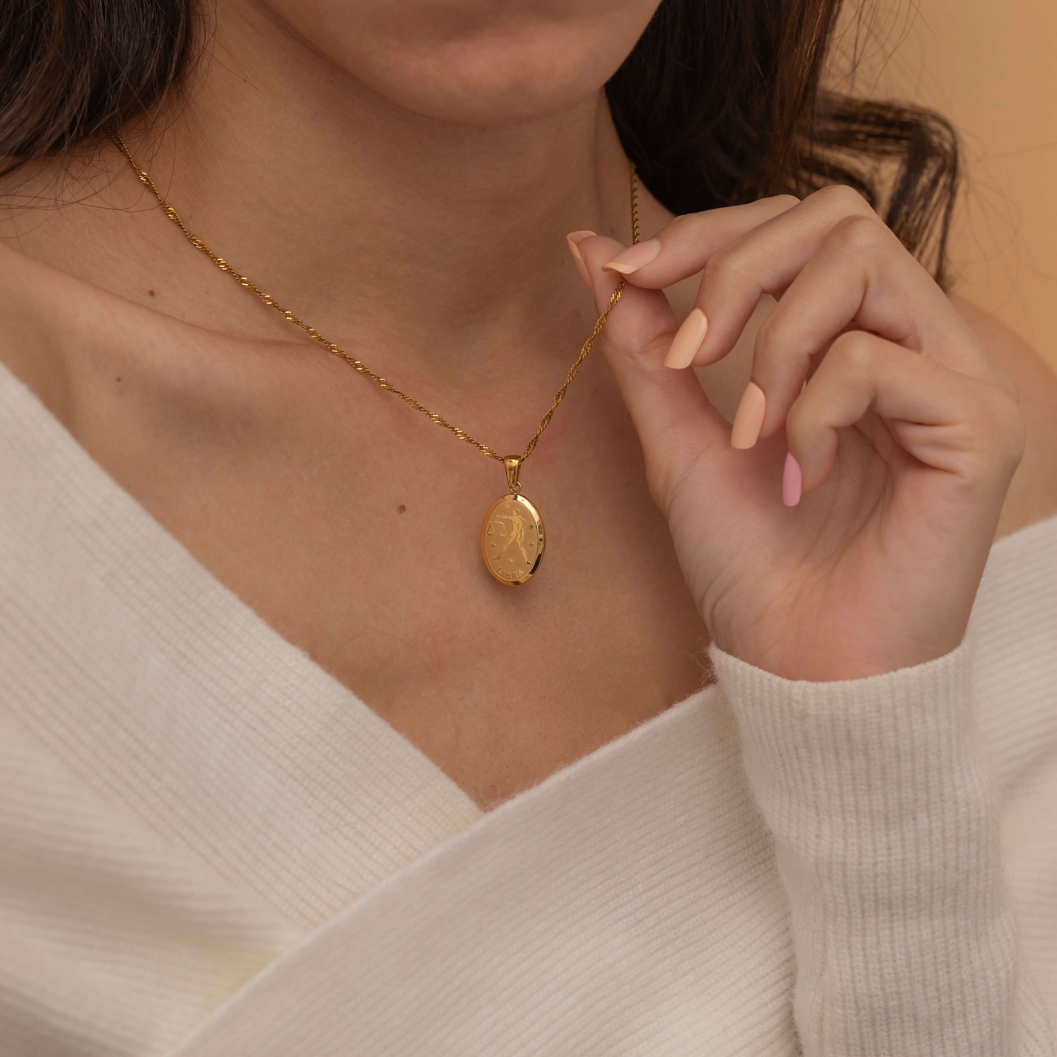 Gold zodiac pendant necklace on a dainty elongated twist chain, featuring an engraved oval charm available in all zodiac signs for personalized style.