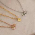 Three custom initial charm necklaces in gold, silver, and rose gold finishes, each with distinct chain styles and personalized round charms on a marble surface.